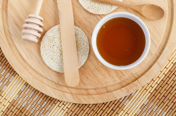 Small glass bowl with honey, wooden spatula and loofah sponges. Natural beauty treatment, sugaring hair removal and homemade spa recipe.Top view, copy space.