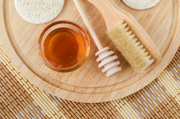 Fototapeta na wymiar Small glass bowl with honey, wooden body brush and loofah sponges. Natural beauty treatment and homemade spa recipe.Top view, copy space.