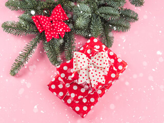 Festive christmas tree fir spruce branch decorated with red and white bows and polka dot wrapped gifts on pink background. Flat lay