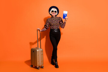 Full size photo of cheerful positive good mood old lady showing tickets passport hold luggage isolated on orange color background