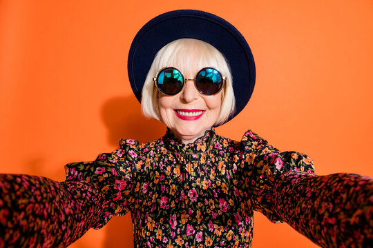 Portrait of happy smiling cheerful positive grandmother take selfie wear sunglasses isolated on orange color background