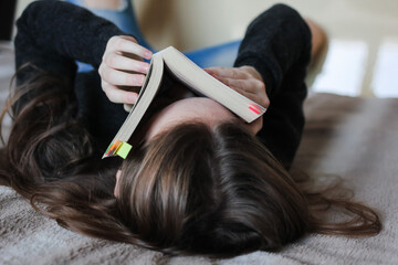 Fototapeta premium Book in the hands of attractive teenage girl reading at home. Concept of education, leisure.