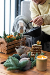 Only hand. A man pours hot tea into a Cup. Still life details in home interior of loggia. Cake  and cup of tea with steam and candle on a coffee table. Breakfast over sofa in winter morning.