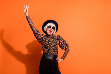 Photo of smiling crazy cheerful happy good mood grandmother raise hand up wear sunglasses isolated on orange color background