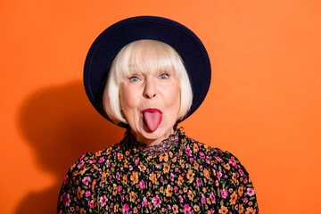 Headshot of sly funny crazy granny showing tongue careless childish playful isolated vibrant orange color background