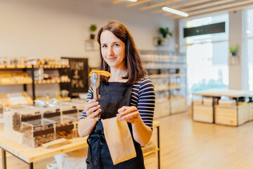 Shop assistant hand put dried mango in paper bag for customer in packaging free shop. Zero waste shopping - woman owner sell fresh at package free grocery store.