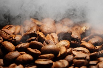 Macro view of freshly roasted fresh Arabica coffee beans with smoke, extreme close up photo of fresh and steamy coffee beans on dark background.