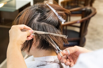 Fototapeta premium Close-up of hair dresser barber cutting hair of female client with scissors and comb