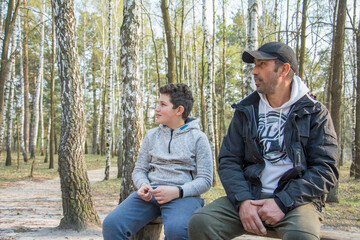 In the spring, on a bright sunny day in the forest, a boy and his dad are sitting on a bench.