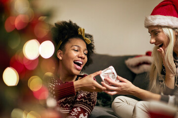 A young girl giving present to female friend at New Year's Eve home party. Xmas, New Year, friends, celebration