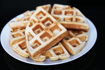 Belgian waffles in white plate on black glass table, top view. Healthy breakfast, pieces of freshly baked classic wafer