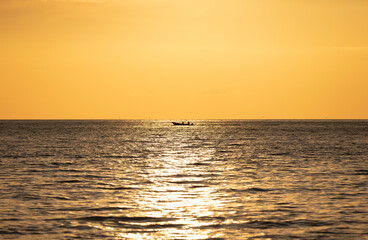 Obraz premium Small boat silhouette on sea horizon during golden hour sunset with shimmering water background