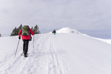 Fototapeta na wymiar Senior couple is snowshoe hiking in alpine snow winter mountains. Allgau, Bavaria, Germany.