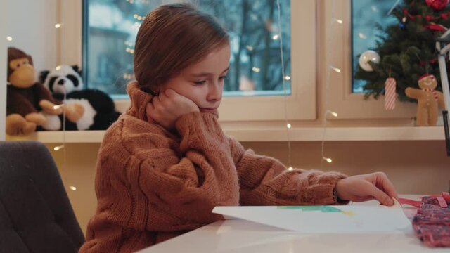 Lonely little girl practicing home study learning distant lessons missing holidays waiting for christmas. Unhappy child. Emotions. Excitement before Christmas time.