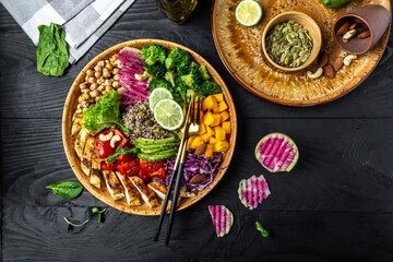 Healthy green vegetable buddha bowl lunch with grilled chicken fillet, quinoa, avocado, pumpkin, tomato, broccoli, red cabbage, chickpea, watermelon radish, fresh lettuce salad, nuts. Top view