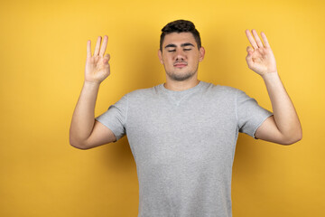 Young handsome man wearing a casual t-shirt over isolated yellow background relax and smiling with eyes closed doing meditation gesture with fingers