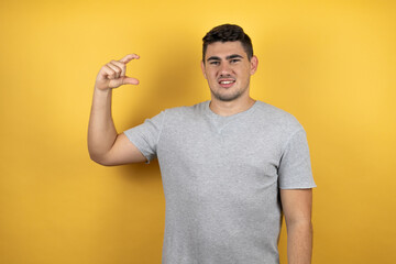 Young handsome man wearing a casual t-shirt over isolated yellow background smiling and confident gesturing with hand doing small size sign with fingers . Measure concept.