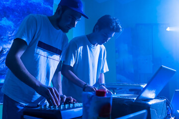 two Disc jockey or DJ stands behind the sound mixing console, makes sound at the party