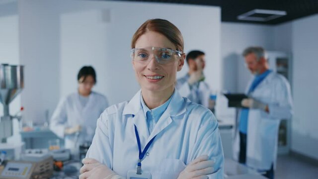 Portrait of woman scientist with protective glasses look at camera smiling. Background team work. Microbiology pharmaceutical biochemistry medical technology. Slow motion
