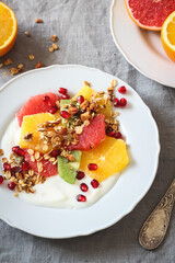 Colorful plate with orange, grapefruit, kiwi slices, homemade granola and yogurt