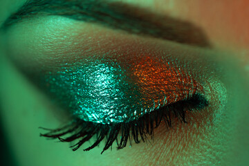 Extreme close up of female eye iris under neon light. Woman with beautiful makeup, glitter shadows...
