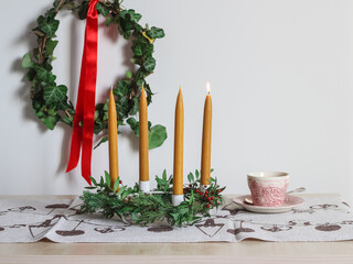 Advent wreath with four candles on the table and one wreath with red ribbon hanging on the wall