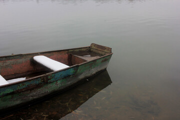 Obraz premium Old shabby boat covered with snow on the winter river
