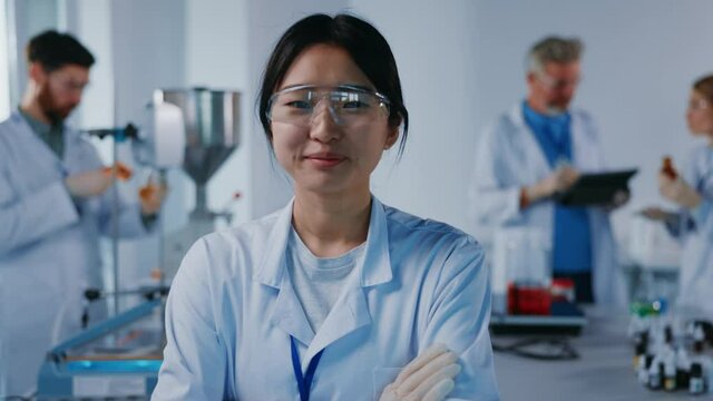 Asian portrait woman scientist with protective glasses look at camera smiling feel happy. Background team work. Microbiology pharmaceutical biochemistry medical technology. Slow motion