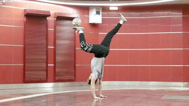 Football freestyle. Young man practices with soccer ball. Professional football freestyler athlete stuffing kicking the ball and making cool tricks walking on hands. Professional healthy  sportman 