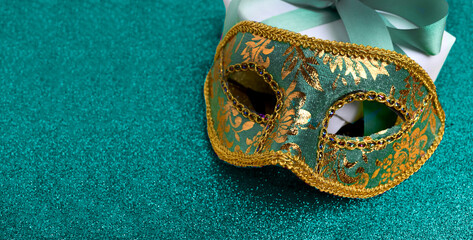 Close up carnival mask, gift box on glitter green background. Christmas, New Year or Mardi gras festive celebration banner with copy space. © Olga