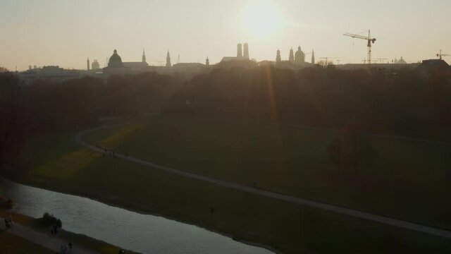 River flowing through English Garden Public Park in Munich with View on City Skyline in beautiful Winter Sunlight, Aerial tilt up Germany