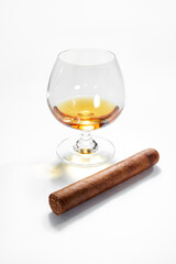 Closed up view of glass of cognac with cigar aside on white back