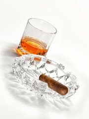 Closed up view of glass of whiskey with cigar and ashtray  white back