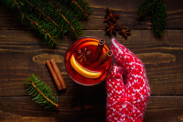 Glass of mulled wine in woman hands on dark wooden table. Knitted wool red mittens