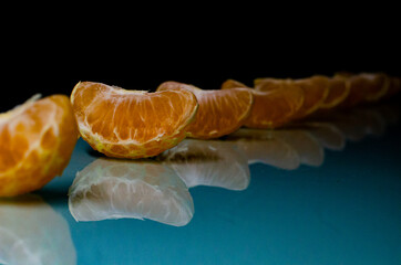 A row of slices of tangerine on the table with a reflection in the dark