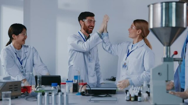 Happy cooperative science team of medical workers successfully developing vaccination or medicine giving high-five applauding celebrating victory in laboratory.