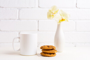 White coffee mug mockup with gentle yellow orchid in vase and cookies