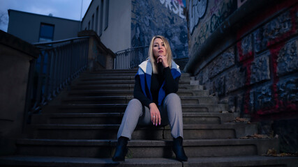 Urban Portrait of a young woman, looking at the Camera, with serious expression, sitting in a staircase in the city.