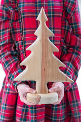 Little girl's hands holding handmade wooden Christmas tree. Child in red tartan dress, close up, selective focus