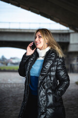 Urban vertical Portrait of a woman talking on the phone in city. She is wearing a winter jacket.