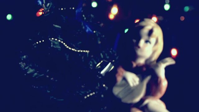 Natale vintage, bambola bambina che suona vicino l'albero di Natale con luci a intermittenza colorate.