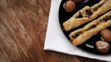 Rollini delicious pastries with mushrooms, champignons and cheese on a black plate on wooden background