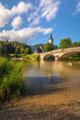 Fototapeta na wymiar Long exposure sunny nature landscape with mountain lake in Slovenia. beautiful lake Bohinj with perfect sky at summer. view on calm lake with azure water, church and stone bridge on background.