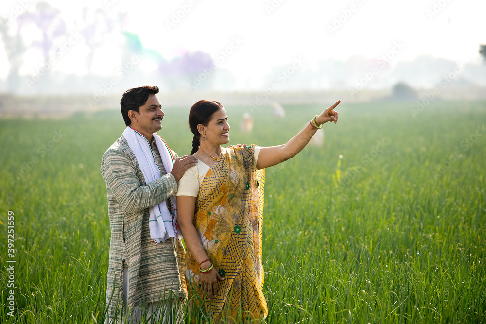 Wall mural Happy Indian couple farmers examining crop in agricultural field