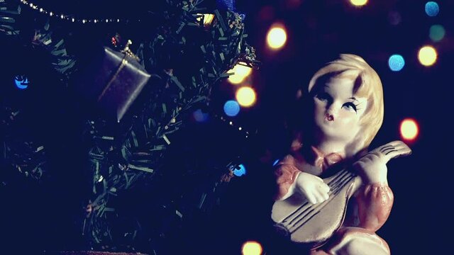 Natale vintage, bambola bambina che suona vicino l'albero di Natale con luci a intermittenza colorate.