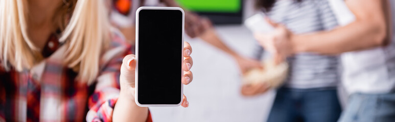 cropped view of woman holding smartphone with blank screen near friends on blurred background, banner