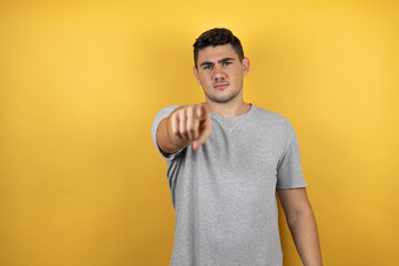 Young handsome man wearing a casual t-shirt over isolated yellow background pointing to the front with finger