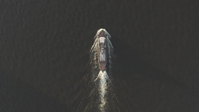 Aerial shot of cargo ship floats on the river or sea. Freight boat carriage goods. Drone fly over moves nautical vessel. Container ship or barge sailing. Transportation by maritime transport. Top view