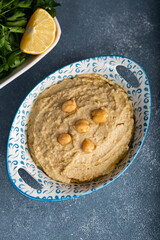 Bowl of homemade hummus on blue background. Humus in bowl decorated with chickpeas and olive oil.