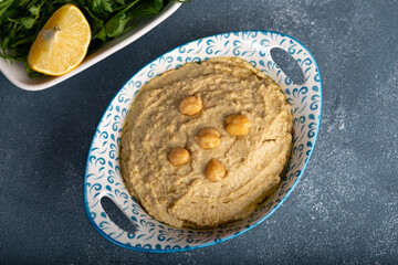 Bowl of homemade hummus on blue background. Humus in bowl decorated with chickpeas and olive oil.